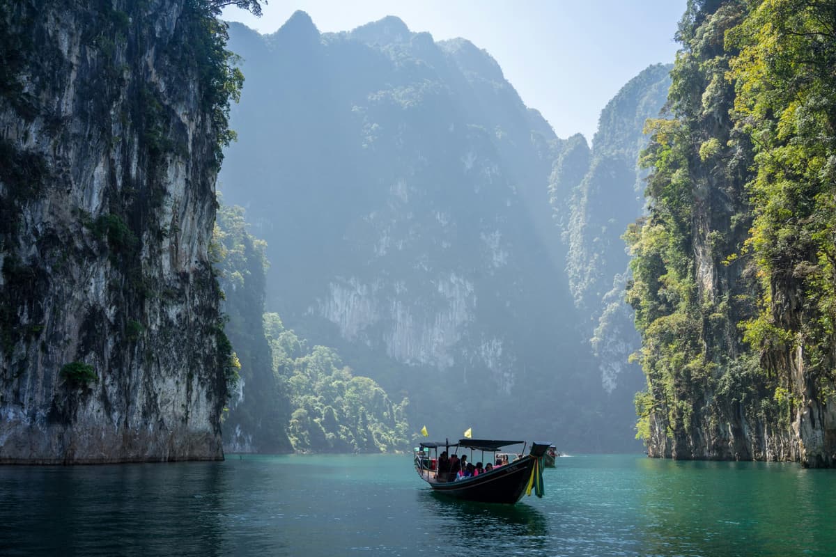 Un bateau long-tail traverse le lac Cheow Lan entre les falaises calcaires, Khao Sok