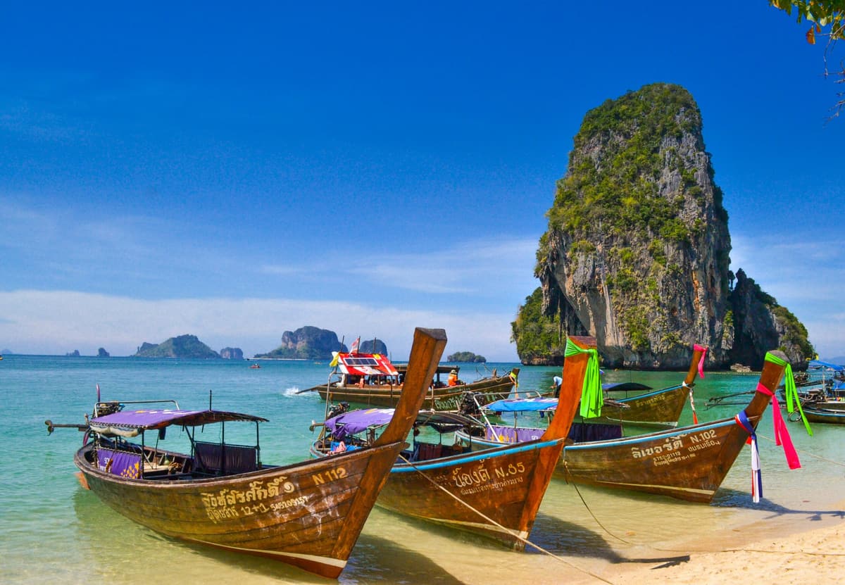 Des bateaux long-tail peints, amarrés sur une plage au pied d’un piton calcaire, Krabi